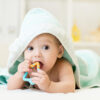 Baby,With,Teether,In,Mouth,Under,Bathing,Towel,At,Nursery