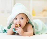 Baby,With,Teether,In,Mouth,Under,Bathing,Towel,At,Nursery