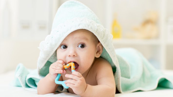 Baby,With,Teether,In,Mouth,Under,Bathing,Towel,At,Nursery